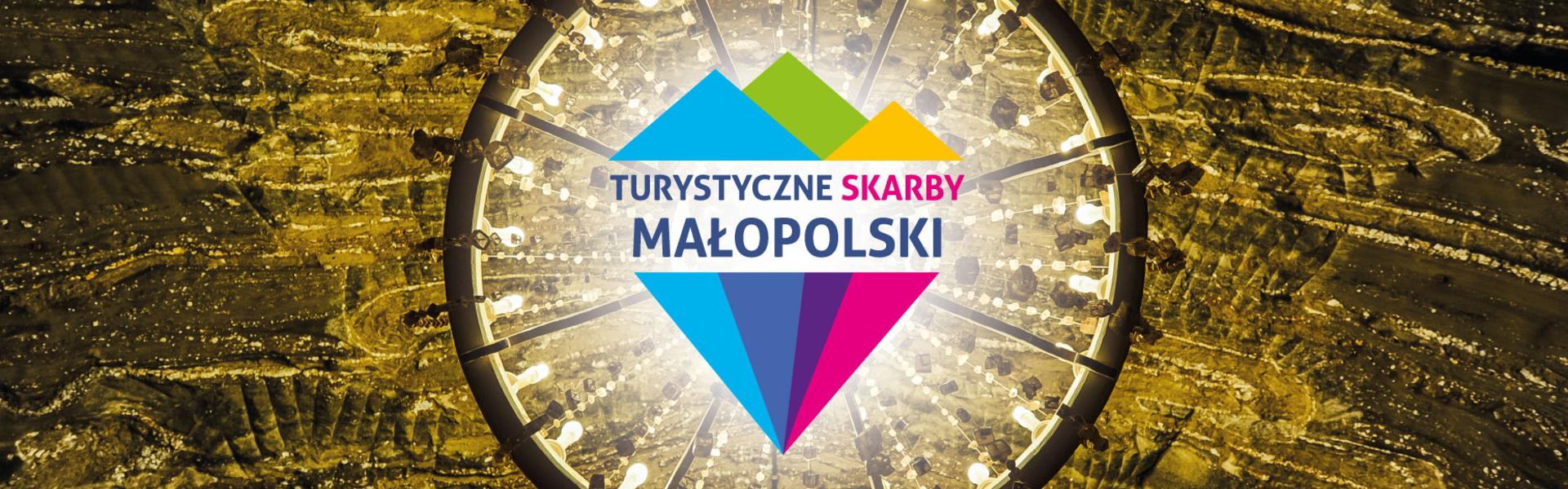 Widok od dołu na żyrandol w Kopalni Soli Bochnia, na środku zdjęcia nałożone logo konkursu Turystyczne Skarby Małopolski, które przypomina kolorowy diament