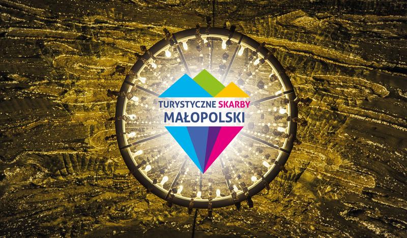 Widok od dołu na żyrandol w Kopalni Soli Bochnia, na środku zdjęcia nałożone logo konkursu Turystyczne Skarby Małopolski, które przypomina kolorowy diament