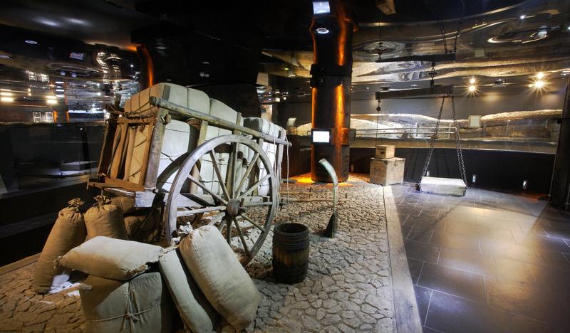 Ekspozycja muzealna - drewniany wóz wyładowany workami, z boku wisi waga.