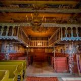 Wnętrze drewnianej cerkwi od strony babińca, nad którym znajduje się chór z drewnianą rzeźbioną balustradą.