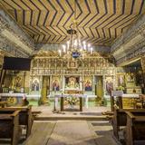 Wnętrze drewnianej cerkwi. Na ścianach polichromie i ikony, w nawie ławki, na wprost ołtarz, za nim piękny ikonostas.