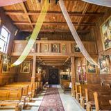 Wnętrze drewnianego kościoła. Nad wejściem chór muzyczny, drewniane ściany, wiszące obrazy, ławy.