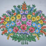 Okrągły bukiet kolorowych, ułożonych regularnie, różnych kwiatów, namalowany na białej ścianie domu.