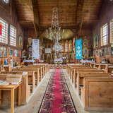 Wnętrze drewnianej cerkwi. Na ścianach ikony, w nawie ławy, na wprost ołtarz i ołtarze boczne oraz ikonostas.