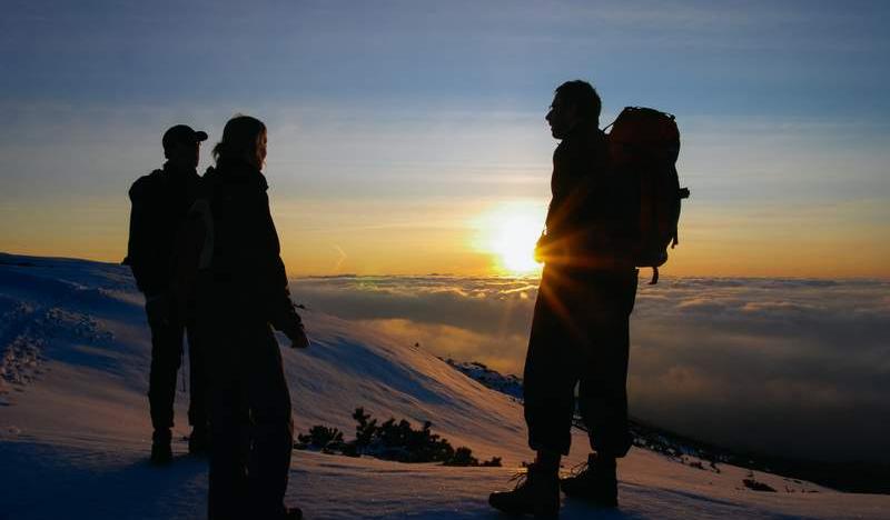 Trzy osoby na szczycie o zachodzie słońca.