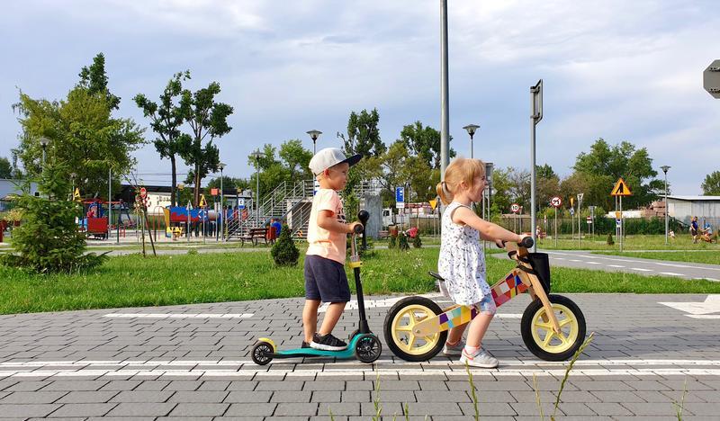 Dwoje dzieci, jedno na hulajnodze, drugie na rowerku.