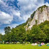 Wysoka jurajska skała (Sokolica), u której stóp na trawie widać rozłożone namioty. Miejsce w Dolinie Będkowskiej.