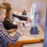 Dzieci w Muzeum Inżynierii i Techniki w Krakowie poznają zasady elektryczności przy jednym z eksponatów muzeum, jakim jest urządzenie wytwarzające prąd, dzięki któremu świecą się żarówki.