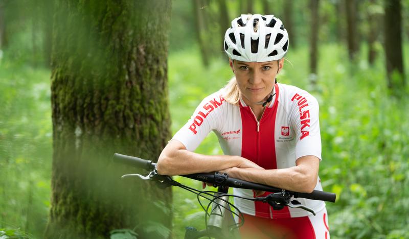 Kobieta w stroju sportowym i kasku na głowie na rowerze w lesie - zdjęcie portretowe.