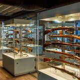 Ułożone w rzędzie szklane gabloty w Muzeum Armii Krajowej w Krakowie ze starą, drewnianą bronią