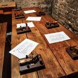 Urządzenia służące do porozumiewania się alfabetem Morse'a leżące na drewnianym stole w Muzeum Armii Krajowej w Krakowie. Za nim kamienna ściana.