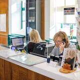 Pracownica punktu informacji turystycznej Zakopane rozmawiająca przez telefon, w tle druga pracownica pracująca na komputerze