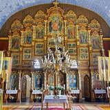 Wnętrze drewnianej cerkwi - ołtarz główny, za nim imponujący ikonostas. Ściany i sufit drewniane, sufit w kolorze niebieskim. Po lewej i prawie stronie stoją ławki dla wiernych, przy nich stoją sztandary z wizerunkami świętych.