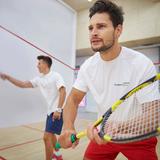 Zdjęcie przedstawia dwóch mężczyzn z rakietami w ręku, którzy grają na korcie w squasha.
