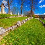 Zielona trawa z kwitnącymi na żółto mniszkami, pośród niej w poprzek wzgórza szeregi kamieni znaczących mogiły poległych, na górze krzyże i drzewa