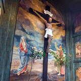 Wnętrze drewnianego kościoła. Na wprost na malowanym dużym obrazie stojącej Matki Bożej i Apostoła wisi duży drewniany krzyż z wiszącą figurą Chrystusa. Po prawej malowane obrazy, pośrodku upadającego Chrystusa pod krzyżem. Po lewej malowany obraz.