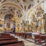 Wnętrze kościoła o bogatym barokowym wystroju. Białe ściany z malowidłami. Ołtarze w kolorze białym i złotym.