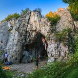 Wejście do jaskini - duży otwór w skale, po której wspinają się osoby w uprzężach i kaskach.