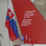 biało-niebiesko-czerwona flaga Słowacji, obok na czerwonym tle napis w języku słowackim
