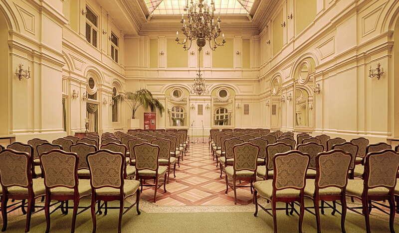 Elegancka sala konferencyjna w Grand Hotelu z kilkoma rzędami wyściełanych krzeseł, widziana od tyłu