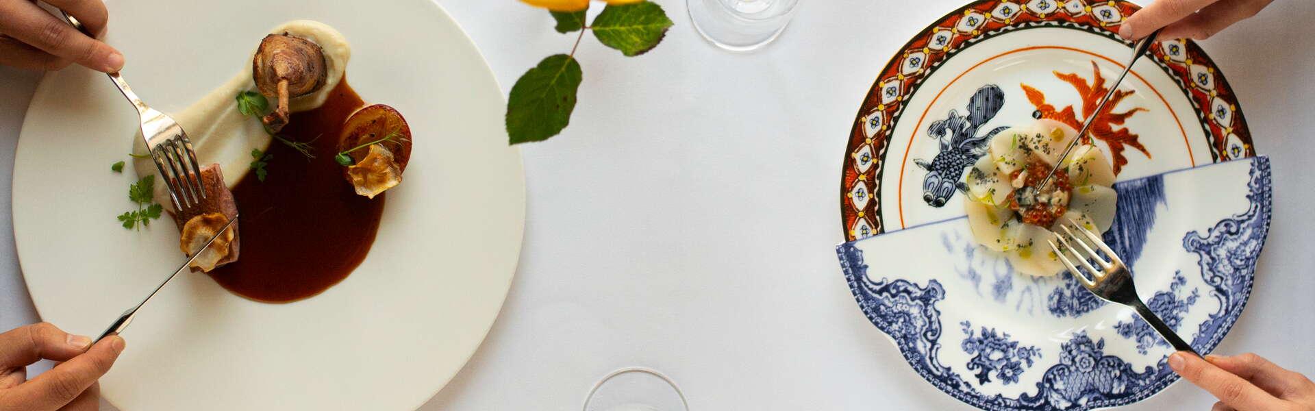 Two plates with elegantly served dishes, a white tablecloth and glasses of wine.