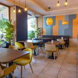 Wnętrze lokalu gastronomicznego, kolorowe żółto-niebieskie ściany, żółte lampy i fotele, brązowe stoliki