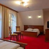 Wnętrze pokoju w Hotelu Dworek Skawiński, dwa podwójne łóżka, stolik z krzesłami, duże okna z udrapowanymi firankami.