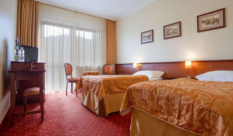 Pokój hotelowy, dwa jednoosobowe, duże łóżka nakryte kolorowymi kapami, stolik, krzesła.