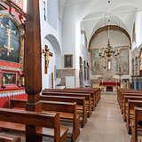 Wnętrze niewielkiego murowanego kościoła. Przed ołtarzem są dwa rzędy drewnianych ławek. Sufit oraz ściany są jasne, na ścianach znajdują się obrazy i inne liturgiczne dekoracje.