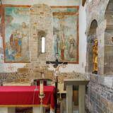 Mały ołtarz w murowanym kościele. We wnętrzu znajduje się stół z czerwonym obrusem, świece, krzyż, na ścianie naprzeciwko malowidło, a po prawej stronie dwie złote rzeźby.