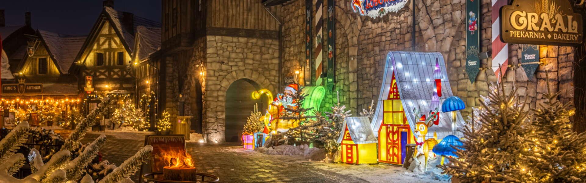 Kamienny budynek lodowiska przed którym stoją oświetlone dekoracje świąteczne, renifer, domek, Święty Mikołaj w parku rozrywki Energylandia podczas Winter Kingdom