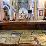 Metalowe tabliczki z podziękowaniami na drewnianej ławce w Kościele pw. Niepokalanego Serca Maryi w Krakowie. W oddali widać zamazane wnętrze kościoła w tym ołtarz.