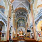 Wysokie wnętrze Kościoła pw. Niepokalanego Serca Maryi w Krakowie w pastelowych barwach. Na środku znajdują się dwa rzędy drewnianych ławek prowadzące prosto do złotego ołtarza. Po obu stronach widać malowane balustrady na piętrze świątyni