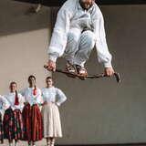 mężczyzna w białym stroju skaczący nad kijkiem, za nim stojące kobiety na scenie w strojach regionalnych 59. Tydzień Kultury Beskidzkiej, Szczyrk, 2022, Dolina Dunajca z Nowego Sącza