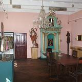 Wnętrze muzeum, m.in. zabytkowe rzeźby, ubrania, figura Chrystusa, ołtarz. Z boku sali stoi drewniany stół z krzesłami.