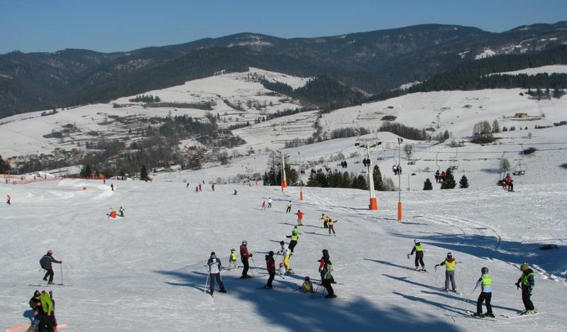 Stok narciarski z narciarzami w Jaworkach z widokiem na Beskid Sądecki.